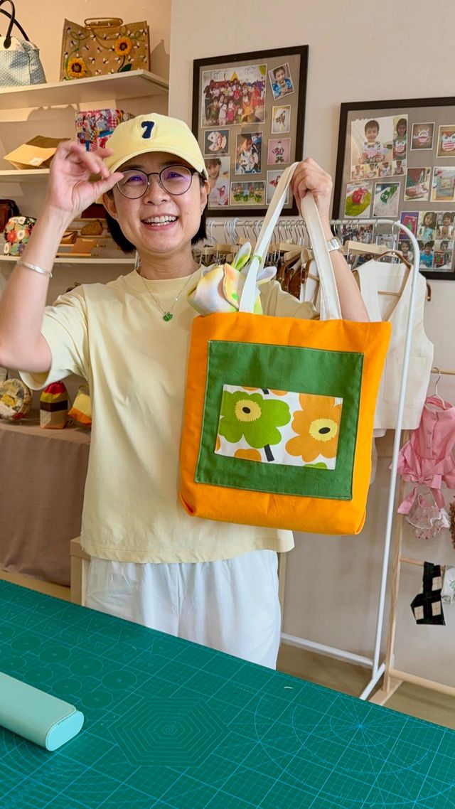 A student holding up an orange-trimmed tote with a green floral panel