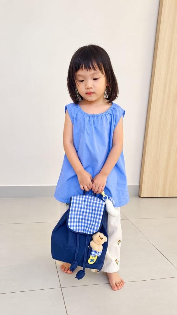 A toddler in a blue top carrying a small navy and gingham backpack
