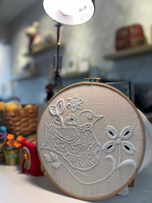 Hand embroidery: a bird and cutwork flower stitched white-on-white on a wooden hoop
